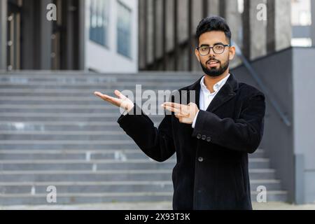 Homme d'affaires indien montrant pointant la zone publicitaire vide pour le texte commercial Copy-space pour la promotion des marchandises à l'extérieur. Arabian Hindu freelance gars dans la rue du centre-ville. Gens d'affaires Banque D'Images