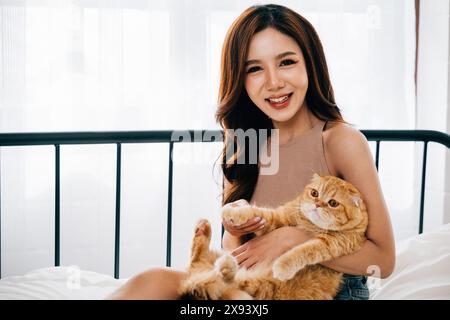 Dans la chambre, une jeune femme sourit avec plaisir tout en tenant son adorable chat Scottish Fold Banque D'Images