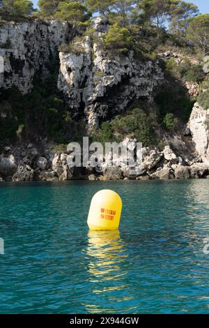 Eau de mer calme avec une bouée jaune au milieu avec l'avertissement "ne pas entrer" et en arrière-plan un mur de roche recouvert de végétation. Backgr maritime Banque D'Images