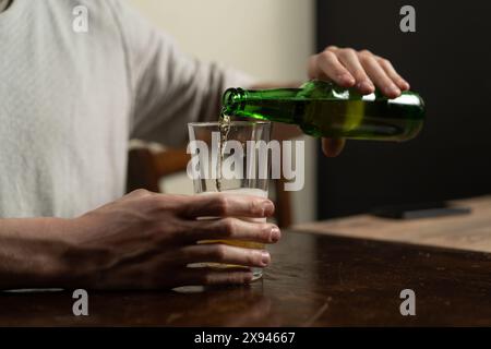 Gros plan d'une personne versant de la bière d'une bouteille verte dans un verre, soulignant l'action et le rafraîchissement de profiter d'une bière à la maison. La scène est CA Banque D'Images