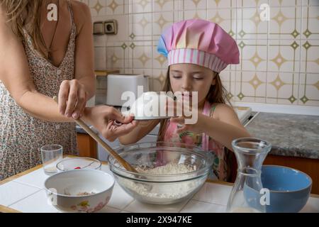 une fille habillée en cuisinière profitant d'un après-midi de cuisine avec sa mère Banque D'Images