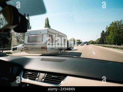 Alsace, France - 19 avril 2019 : une voiture remorquant une caravane sur une autoroute très fréquentée, capturée de l'intérieur d'un autre véhicule, avec des arbres et un ciel dégagé en arrière-plan. Banque D'Images