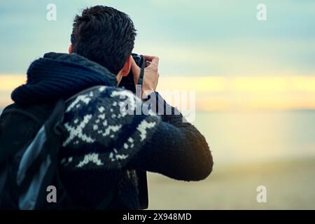 Plage, homme et photographie au coucher du soleil en vacances, voyage ou vacances d'été en Espagne. Photo reflex numérique, vue arrière ou personne à l'extérieur de l'océan pour Banque D'Images