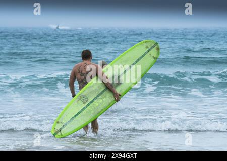 Un surfeur portant sa planche de surf courant dans la mer pour participer à la compétition de surf Sand Bandit Showdown au GT Western Great Western Beach dans le N. Banque D'Images