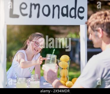 Limonade, enfant et vente pour fille, stand et signe pour petite entreprise, verres et heureux. Extérieur, pelouse et nutrition des boissons, sourire et enfant dans Banque D'Images