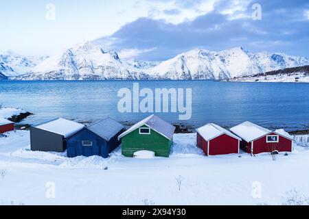 Rorbu en bois coloré recouvert de neige dans le paysage glacé par le fjord, Djupvik, Olderdalen, Lyngen fjord, Lyngen Alpes, Troms og Finnmark, Norvège Banque D'Images