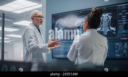 Réunion de laboratoire de l'hôpital de neurosciences médicales : équipe diversifiée de neurochirurgiens et de neurologues analyser l'écran de télévision montrant l'IRM avec des images de cerveau, parler de la méthode de traitement des patients malades, de la guérison de nouveaux médicaments Banque D'Images