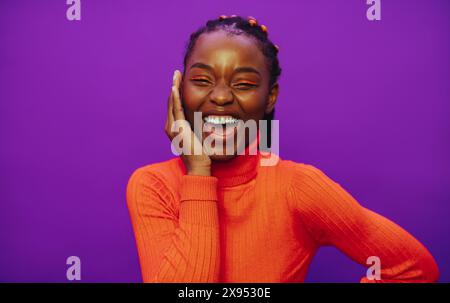 Femme noire confiante avec des cheveux tressés bicolores, portant des vêtements décontractés et un col polo élégant. Elle se tient sur un fond violet éclatant. Banque D'Images