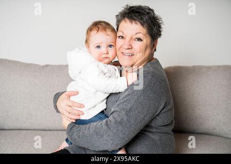 Heureuse petite fille positive assise sur les genoux de grand-mère Banque D'Images