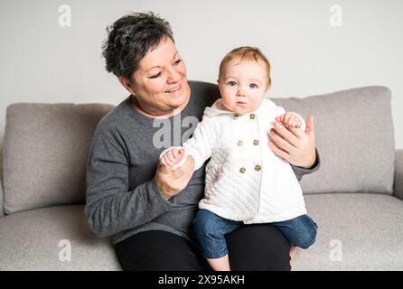 Heureuse petite fille positive assise sur les genoux de grand-mère Banque D'Images