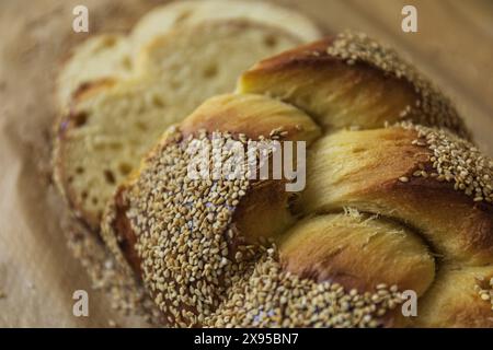 Pain Challah traditionnel tressé maison sur papier cuisson décoré de graines de sésame, boulangerie juive traditionnelle tranchée pour le Shabbat, gros plan sur la vie supérieure Banque D'Images