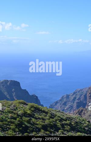 Vue imprenable sur les montagnes verdoyantes rencontrant le vaste océan bleu sous un ciel dégagé avec des nuages lointains Banque D'Images