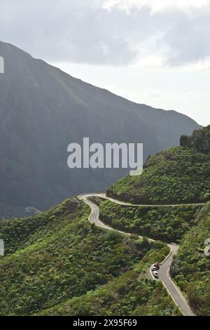 Route de montagne sinueuse et pittoresque à travers des collines verdoyantes avec en toile de fond spectaculaire de pics imposants sous un ciel partiellement nuageux Banque D'Images