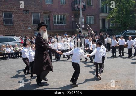 Un rabbin et ses élèves dansent lors d'une célébration du Lag B'Omer dans une rue fermée à Williamsburg, Brooklyn, New York. Banque D'Images