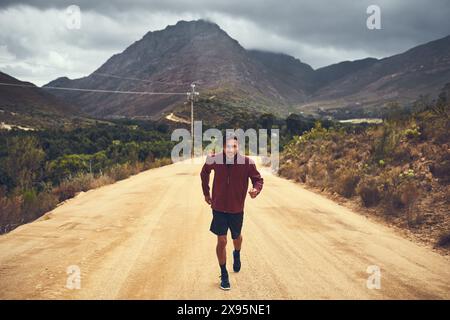 Fitness, portrait et homme dans la nature pour la course à pied, l'exercice et l'aventure sportive en Suisse. Extérieur, chemin de terre et nuages avec coureur masculin pour Banque D'Images