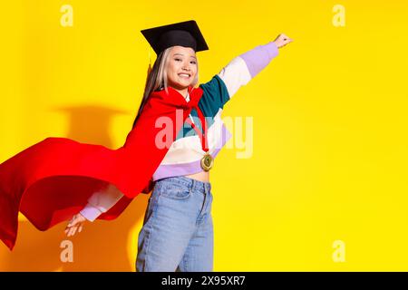 Photo de la femme positive optimiste chinoise porter le chapeau académique de manteau rouge tenir le poing levant isolé sur fond de couleur jaune vibrant Banque D'Images