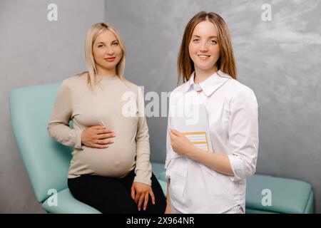 Jeune femme enceinte assise sur la chaise gynécologique lors d'une consultation médicale avec un gynécologue. Le médecin tenant la carte médicale du patient Banque D'Images