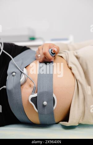 Femme enceinte vérifiant le rythme cardiaque fœtal par surveillance fœtale. Mère enceinte avec sage-femme qui ajuste les capteurs hors cardiotocographie (CTG). Banque D'Images