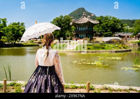 Corée du Sud, Séoul. Femme en hanbok. Jardin du parc du palais de Gyeongbokgung. Pavillon Hyangwonjeong en arrière-plan. Tradition vestimentaire coréenne. Banque D'Images