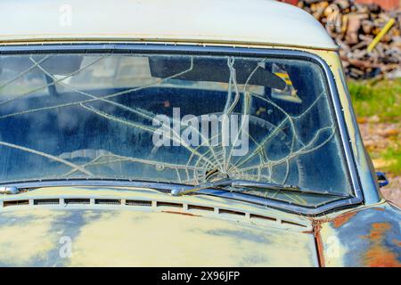 Vue en coupe avant supérieure d'une voiture d'époque altérée, mettant l'accent sur le pare-brise de la voiture avec un motif de fissures en toile d'araignée. Banque D'Images