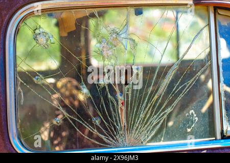 Vue rapprochée de la vitre latérale d’une vieille voiture qui a été brisée et recouverte de multiples fissures émanant de plusieurs points d’impact. Voiture d'époque R Banque D'Images