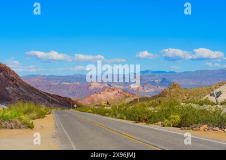 Vue panoramique d'une route qui s'étend à travers un paysage désertique du Nevada avec des collines rocheuses, une végétation clairsemée et des chaînes de montagnes au loin sous un Banque D'Images