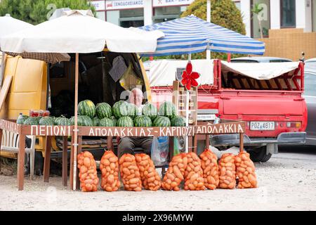 Rhodes Grèce. Un étal en bord de route vendant des pastèques fraîches et des pommes de terre cultivées localement. Le détenteur de la stalle sourit en étant assis à sa stalle du marché Banque D'Images