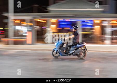 Un homme conduisant un scooter à grande vitesse le long de la route la nuit. Le plan est panoramique donnant une impression de mouvement. Rhodes, Grèce Banque D'Images