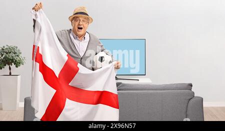 Fan de football âgé tenant un drapeau anglais et soutenant une équipe depuis chez lui Banque D'Images