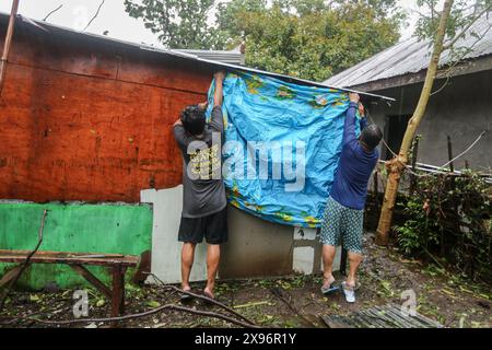 Laguna, Calabarzon, Philippines. 28 mai 2024 : les hommes philippins essayant de protéger la maison endommagée de la pluie avec les moyens à portée de main comme piscine gonflable. Le typhon Ewiniar (nom philippin Aghon) a laissé derrière lui au moins 7 morts, des centaines de maisons endommagées et des milliers de personnes évacuées de leurs maisons. Cette première tempête de 2024 est venue après des mois de chaleur brûlante provoquée par le phénomène long El Nino. Prévue depuis trop longtemps comme dépression tropicale par PAGASA (pH Weather), son intensité a surpris de nombreux Philippins non préparés, causant beaucoup de destructions et de dégâts. Crédit : Kevin Izorce/Alamy Live News Banque D'Images