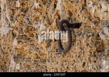 Un anneau de cravate en métal rouillé pour sécuriser les chevaux, coincé dans le mur d'une vieille maison en briques calcaires en Israël. Banque D'Images