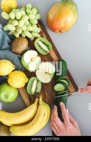 Les mains féminines méconnaissables coupent le concombre sur une planche à découper dans la cuisine. Pose à plat. Banque D'Images