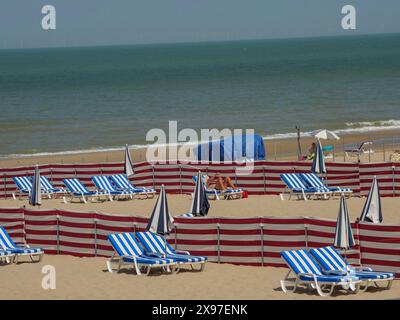 Plage avec plusieurs chaises longues rayées bleues et blanches et parasols, pavée de cloisons rouges et surplombant la mer, chaises longues colorées Banque D'Images