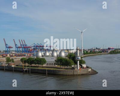 Vue sur le port avec centrale éolienne, réservoirs sphériques, conteneurs et arbres verts sous un ciel dégagé, belle ville sur la rivière avec port Banque D'Images