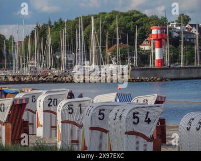 Ambiance de vacances à la côte avec des chaises de plage blanches et un phare rouge vif et blanc en face des voiliers, port avec des voiliers Banque D'Images