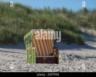 Une seule chaise de plage verte avec des rayures jaunes et blanches se dresse sur la plage en face d'une dune herbeuse, plage de la mer du Nord avec des chaises de plage colorées Banque D'Images