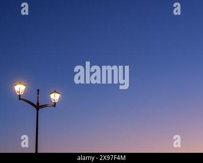 Un lampadaire brille contre un ciel bleu foncé au crépuscule, coucher de soleil dans de nombreuses couleurs sur une plage avec une mer calme, de haan, belgique Banque D'Images