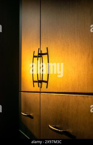 Armoires à tiroirs en bois avec poignées en métal - mise au point sélective. Rayons du soleil du soir avec des rayons de soleil perçant à travers la fenêtre. Banque D'Images