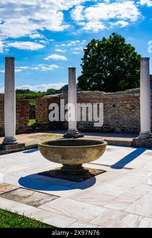 De hautes colonnes blanches se dressent au milieu d'anciennes ruines de briques à Felix Romuliana, en Serbie, avec des arbres verts en arrière-plan et un ciel bleu clair au-dessus de lui Banque D'Images