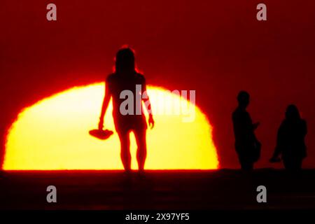 Île de Palms, États-Unis. 29 mai 2024. Les gens silhouettés par le lever du soleil, marchent le long de la plage tandis qu'une vague de chaleur balaye la région apportant des températures dans les années 90, 29 mai 2024 à Isle of Palms, Caroline du Sud. Crédit : Richard Ellis/Richard Ellis/Alamy Live News Banque D'Images