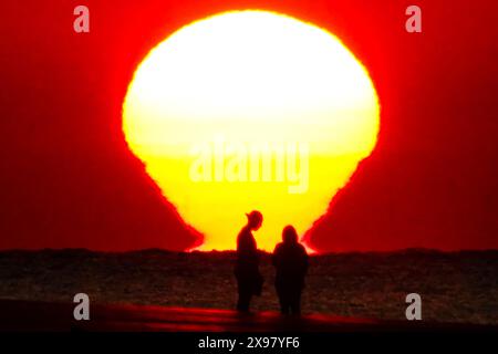 Île de Palms, États-Unis. 29 mai 2024. Le soleil se lève sur l'océan Atlantique reflété sur l'eau silhouettant un couple sur la plage alors qu'une vague de chaleur balaie la région apportant des températures dans les années 90, 29 mai 2024 à l'île de Palms, Caroline du Sud. Crédit : Richard Ellis/Richard Ellis/Alamy Live News Banque D'Images