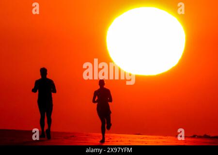 Île de Palms, États-Unis. 29 mai 2024. Les gens silhouettés par le lever du soleil, jogging le long de la plage alors qu'une vague de chaleur balaye la région, apportant des températures dans les années 90, 29 mai 2024 à Isle of Palms, Caroline du Sud. Crédit : Richard Ellis/Richard Ellis/Alamy Live News Banque D'Images