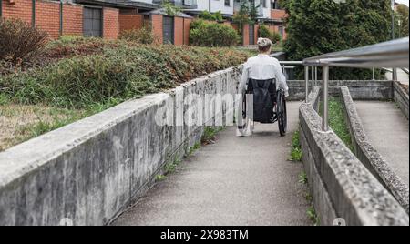 Personne ayant une déficience physique conduisant un fauteuil roulant le long d'une rampe accessible pour accéder à la rue. Handicap et concepts de mobilité. Banque D'Images