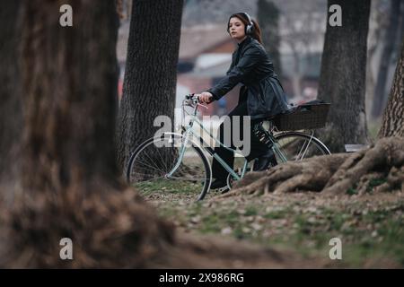 Élégante jeune femme d'affaires avec des écouteurs à vélo dans un parc Banque D'Images