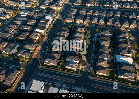 Vue aérienne en fin d'après-midi des rues bordées de maisons australiennes modernes en placage de briques de taille similaire dans la banlieue en pleine croissance de Sydney. Banque D'Images