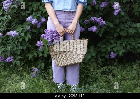 Belle jeune femme tenant un sac en osier avec bouquet de fleurs de lilas dans le parc le jour du printemps, gros plan Banque D'Images