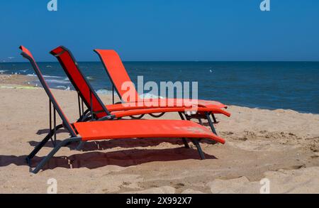 Chaises longues rouges sur la plage. Personne sur les chaises longues. chaise longue rouge sur une plage de sable peu profonde, équipement de plage. Banque D'Images