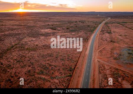 Vue aérienne d'une longue route traversant des plaines arides vers le coucher du soleil à Broken Hill dans l'outback de la Nouvelle-Galles du Sud, Australie. Banque D'Images