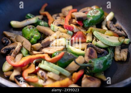 Mélange coloré de légumes sautés dans une poêle : champignons tranchés, courgettes, poivrons rouges, jaunes et verts, légumes cuits utilisés dans un plat sain Banque D'Images