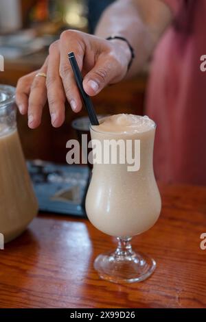 Barman ou mixologue ajoutant la touche finale à un cocktail alcoolisé tel que la pina colada servie dans un verre en forme de tulipe, boisson fraîchement préparée Banque D'Images